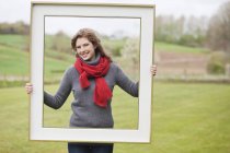 Портрет усміхненої жінки, що стоїть з рамкою в парку — стокове фото