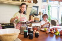 Nonna cucina cibo e bambino peeling una mela a casa — Foto stock