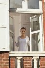 Mujer joven abriendo ventana en apartamento - foto de stock
