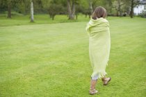 Девушка, завернутая в зеленое одеяло, ходит по полю — стоковое фото