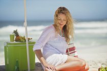 Entspannte blonde Frau sitzt am Strand — Stockfoto