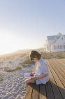 Little girl sitting on boardwalk on sandy beach and reading book — Stock Photo
