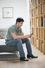 Homem sentado no sofá e lendo livro eletrônico em casa — Fotografia de Stock