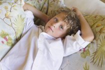 Портрет маленького хлопчика з кучерявим волоссям, що лежить на дивані — стокове фото