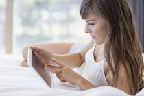 Giovane donna sdraiata sul letto e utilizzando tablet digitale — Foto stock