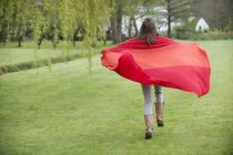 Ragazza avvolta in una coperta rossa che cammina nel campo — Foto stock