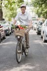 Man carrying vegetables in basket while riding bicycle — Stock Photo