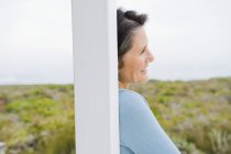 Primer plano de sonriente mujer día soñando mientras se apoya en el poste en la naturaleza - foto de stock