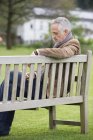 Elegante uomo maturo utilizzando il telefono cellulare su panchina in legno nel parco — Foto stock