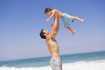 Man playing with son on beach under blue sky — Stock Photo