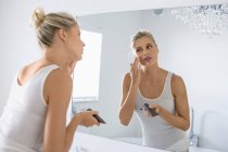 Blond young woman applying moisturizer on face in bathroom — Stock Photo