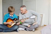 Teenage boy learning guitar with his father at home — Stock Photo