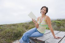 Laughing woman sitting on boardwalk in nature with book — Stock Photo