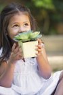 Cute little girl holding potted plant and looking up outdoors — Stock Photo