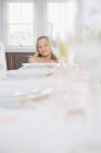 Retrato de uma menina sorridente sentada na mesa de jantar servida — Fotografia de Stock
