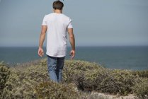 Вид сзади на молодого человека, идущего по берегу моря — стоковое фото