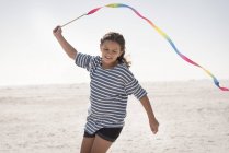 Glückliches Mädchen spielt mit buntem Band am Strand — Stockfoto