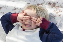 Playful little boy lying down and covering eyes with hands — Stock Photo