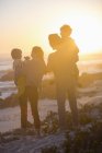 Rückansicht einer glücklichen Familie, die bei Sonnenuntergang am Strand steht und die Aussicht betrachtet — Stockfoto