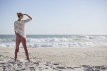 Alta jovem mulher de pé na praia ensolarada — Fotografia de Stock