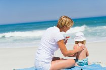 Donna che applica lozione abbronzatura a sua figlia sulla spiaggia — Foto stock