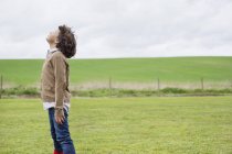 Мальчик мечтает в зеленом поле под облачным небом — стоковое фото