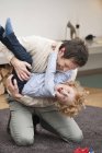 Homem alegre brincando com o filho no tapete em casa — Fotografia de Stock