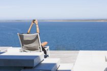 Donna irriconoscibile seduta sulla sedia sulla riva del lago e scattare selfie con smartphone — Foto stock