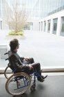 Hombre de negocios discapacitado sentado en silla de ruedas frente al edificio de oficinas - foto de stock