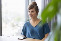 Close-up of smiling young woman sitting at table next to window — Stock Photo