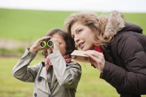 Boy looking through binoculars while standing with mother in countryside — Stock Photo