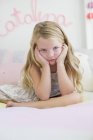 Portrait of cute little girl sitting on bed with head in hands — Stock Photo