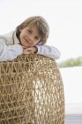 Portrait of smiling little boy leaning on wicker chair — Stock Photo