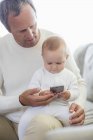 Pai feliz e bebê filha brincando com telefone celular no sofá — Fotografia de Stock