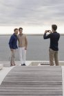 Людина фотографує друзів з мобільним телефоном на дерев'яній терасі на озері — стокове фото