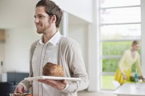 Sorrindo homem carregando pão na bandeja em casa — Fotografia de Stock