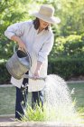 Donna in cappello di paglia irrigazione piante nel giardino estivo — Foto stock
