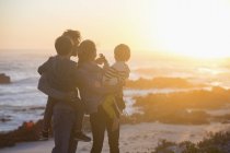 Happy family standing on beach at sunset and looking at view — Stock Photo