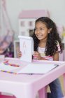 Счастливая маленькая девочка показывает рисунок за розовым столом — стоковое фото