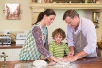 Милый маленький мальчик и его родители смешивают тесто на кухне — стоковое фото