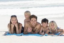 Retrato de familia feliz acostada sobre una manta en la playa - foto de stock