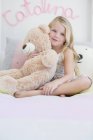 Ritratto di bambina carina sorridente che tiene orsacchiotto sul letto — Foto stock