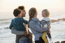 Família feliz em pé na praia ao pôr do sol — Fotografia de Stock