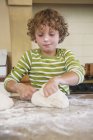 Cute little boy kneading dough in kitchen — Stock Photo