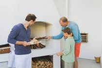 Two men with a boy cooking kebab at fireplace — Stock Photo