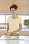 Portrait of woman in patterned t-shirt cutting pineapple on chopping board in kitchen — Stock Photo