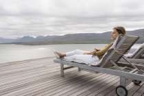 Elegant young woman relaxing on deckchair at lake shore — Stock Photo