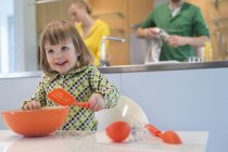 Niedliches kleines Mädchen mit Schlitzlöffel und Rührschüssel in der Küche — Stockfoto