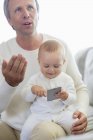 Happy father and baby daughter playing with mobile phone on couch — Stock Photo