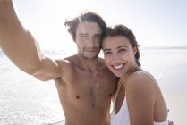 Porträt eines glücklichen jungen Paares beim Selfie am sonnigen Strand — Stockfoto